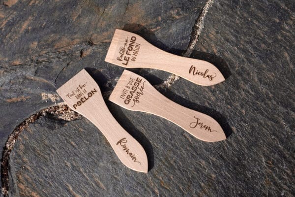 Lot de spatules à raclette en bois personnalisées avec gravure de prénoms et phrases humoristiques.