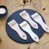 Lot de spatules à raclette en bois personnalisées avec gravure de prénoms et phrases humoristiques.