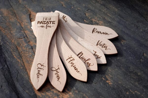 Lot de spatules à raclette en bois personnalisées avec gravure de prénoms et phrases humoristiques.